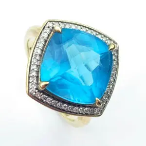 Close-up of a gold ring featuring a large blue pear-shaped gem surrounded by a halo of small diamonds.