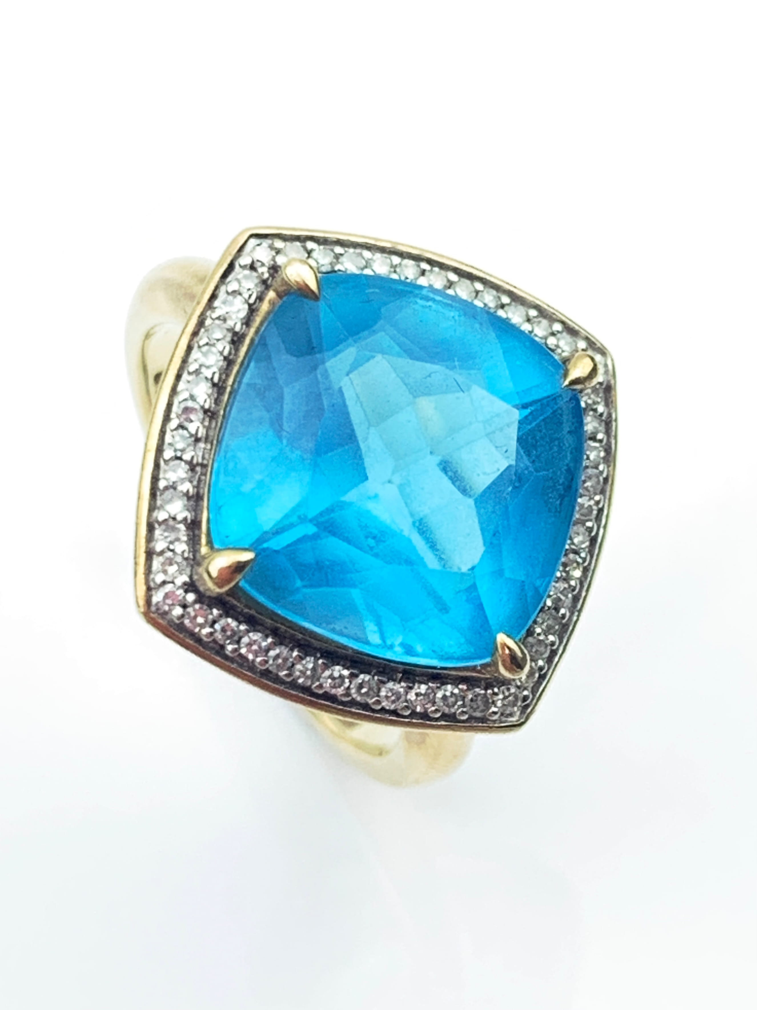 Close-up of a gold ring featuring a large blue pear-shaped gem surrounded by a halo of small diamonds.