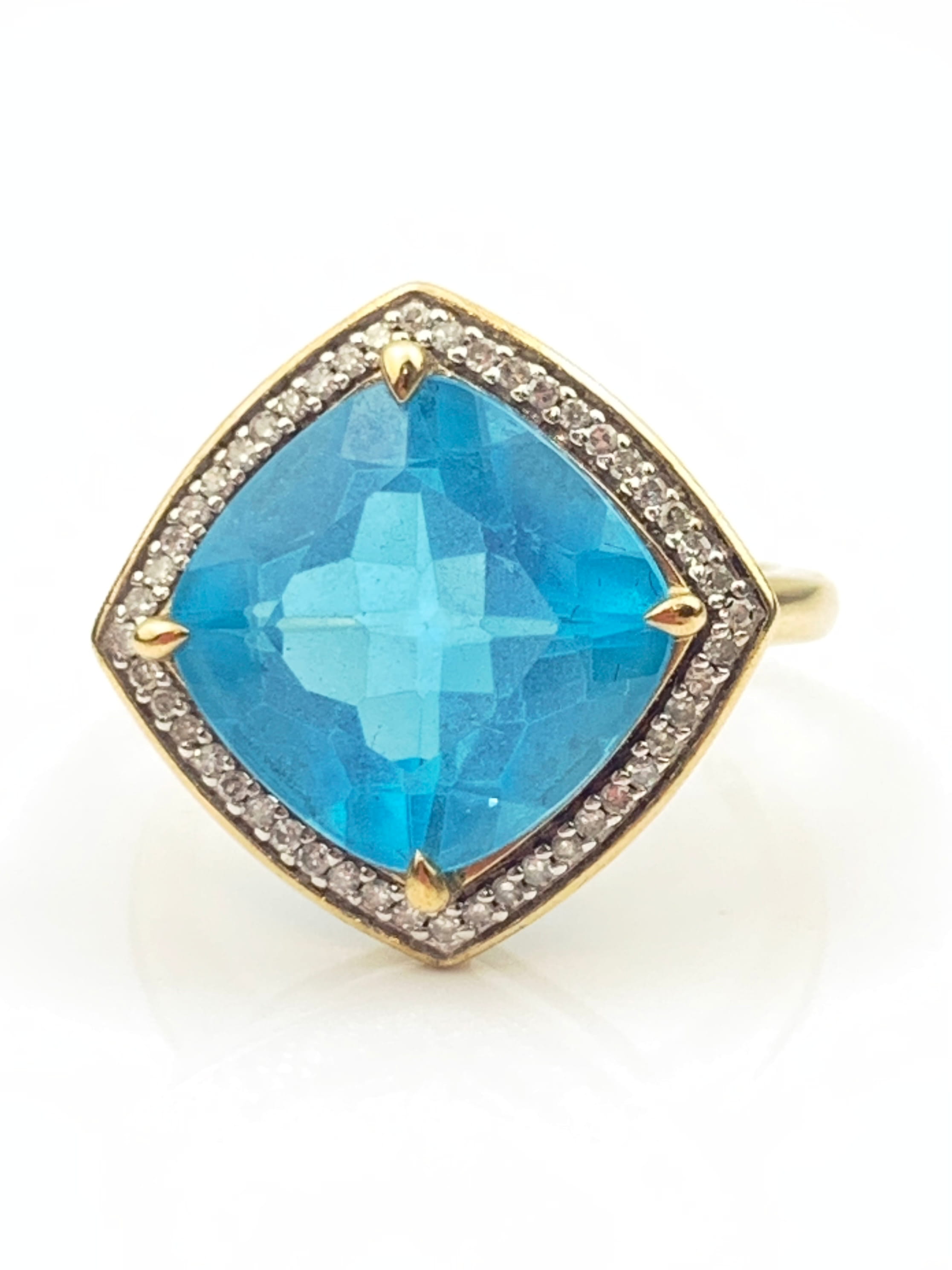 Gold ring featuring a large cushion-cut blue gemstone with a diamond halo around the setting.