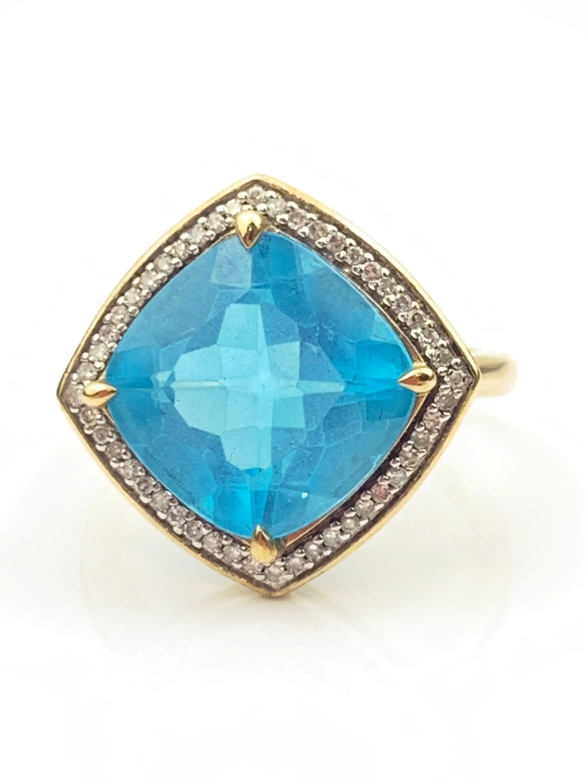 Gold ring featuring a large cushion-cut blue gemstone with a diamond halo around the setting.
