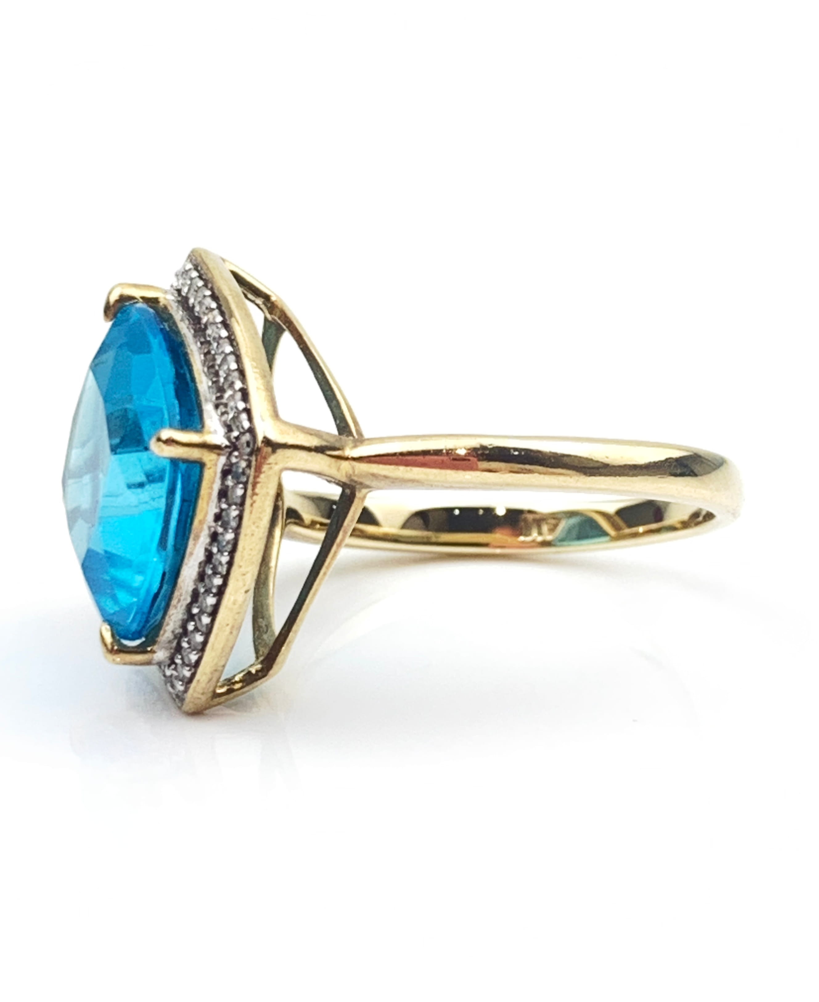 Gold ring with a large blue gemstone and diamond-accented band on a white background, close-up view