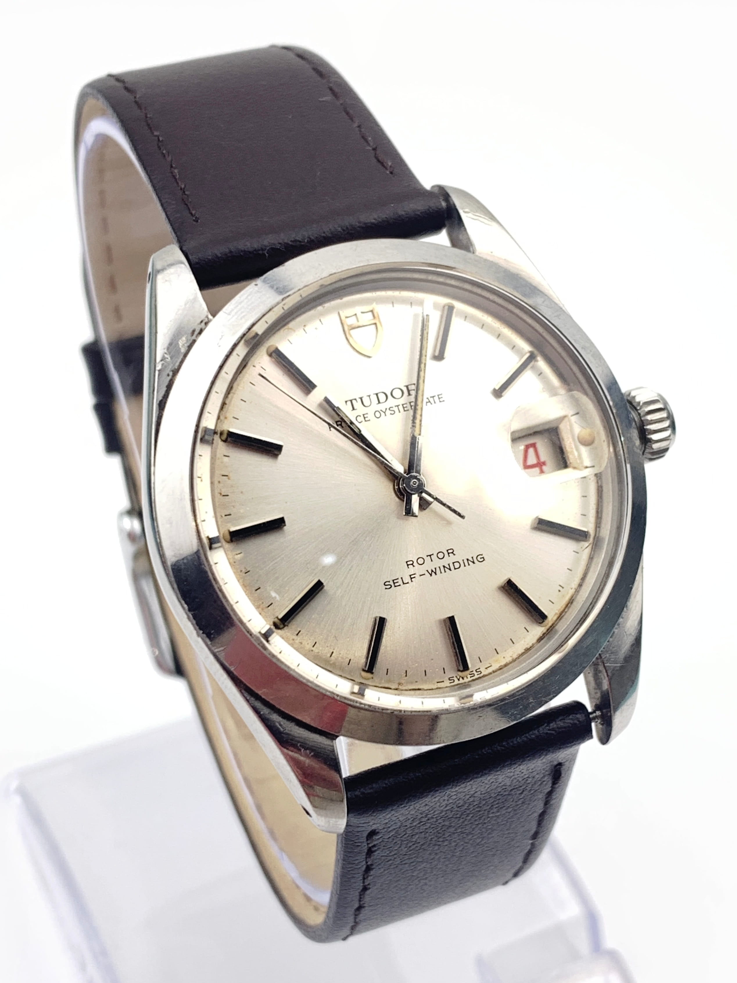 Close-up of a Tudor wristwatch with a silver dial, black hour markers, and a black leather strap.