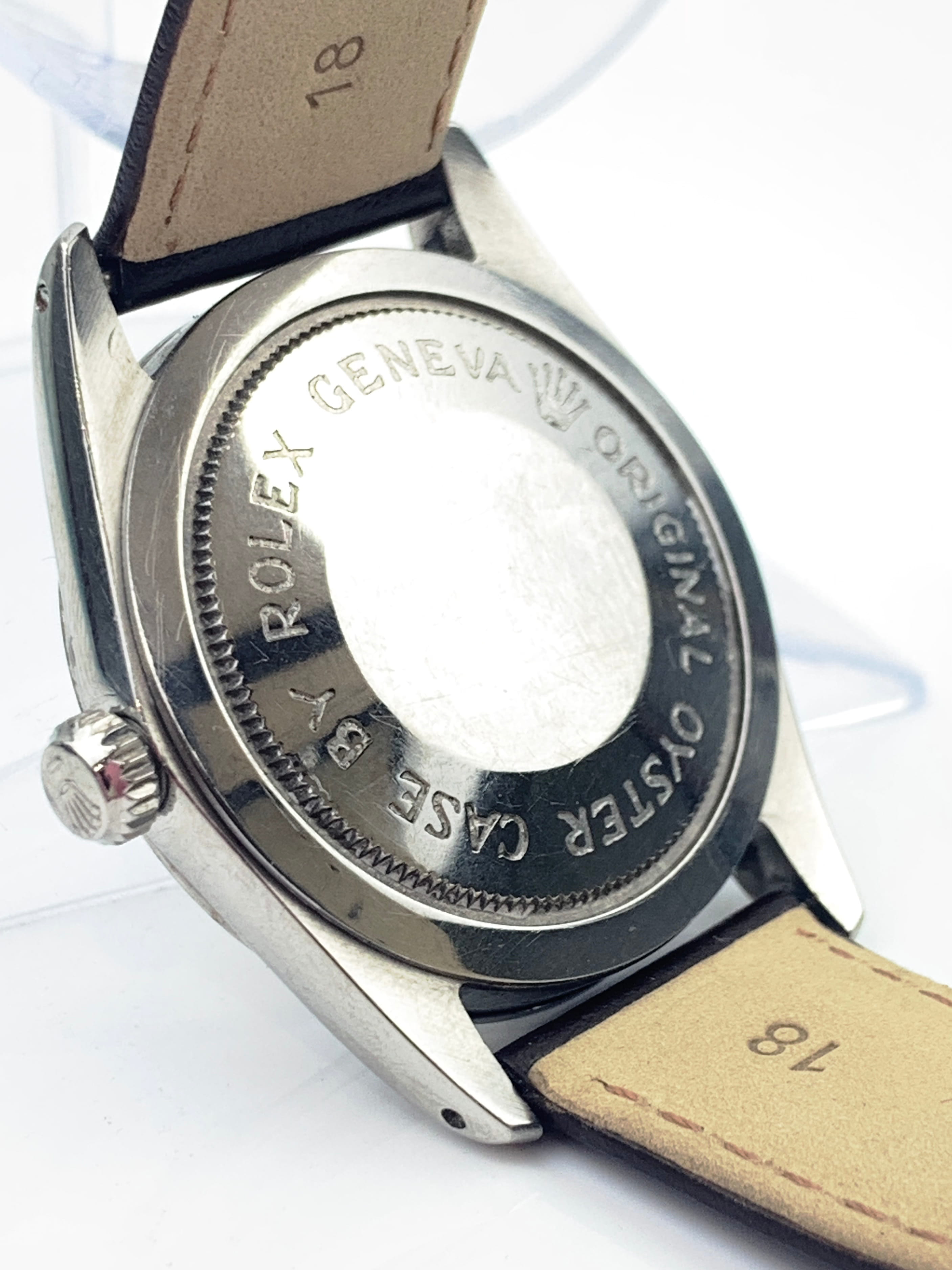 Close-up of a stainless steel watch back with ROLEX GENEVA engraving and a tan leather strap attached.